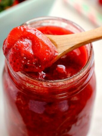 zoomed in view of a wooden spoon being dipped into a jar of strawberry topping