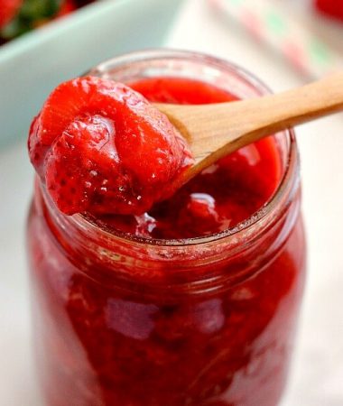 zoomed in view of a wooden spoon being dipped into a jar of strawberry topping