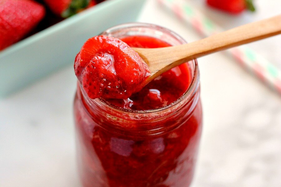 zoomed in view of a wooden spoon being dipped into a jar of strawberry topping