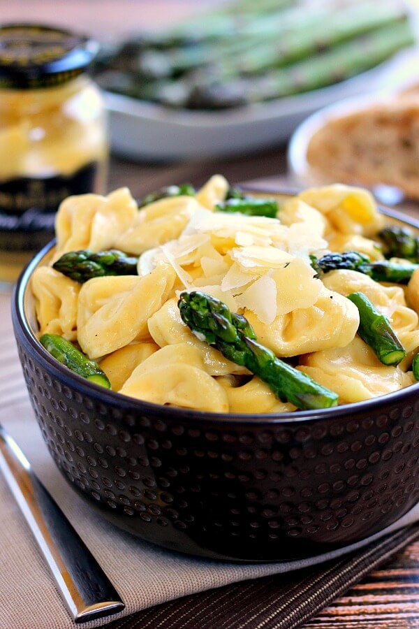 a bowl of tortellini in cream sauce. fresh asparagus and a jar of mustard rest in the background. 