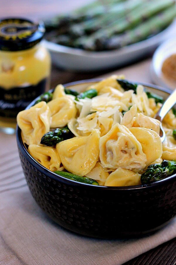 a bowl of tortellini in cream sauce. fresh asparagus and a jar of mustard rest in the background. 