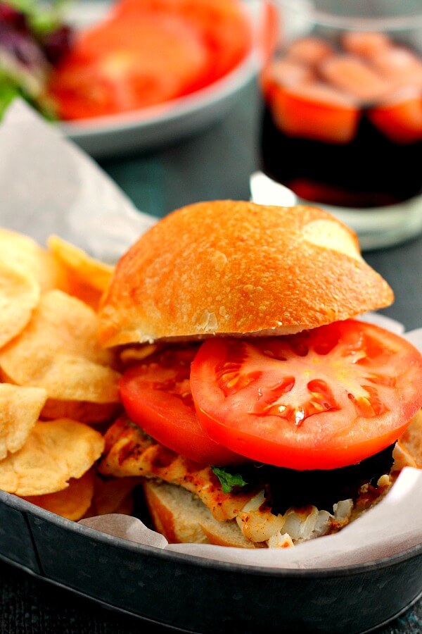 A grilled haddock sandwich on in a sandwich boat with potato chips.