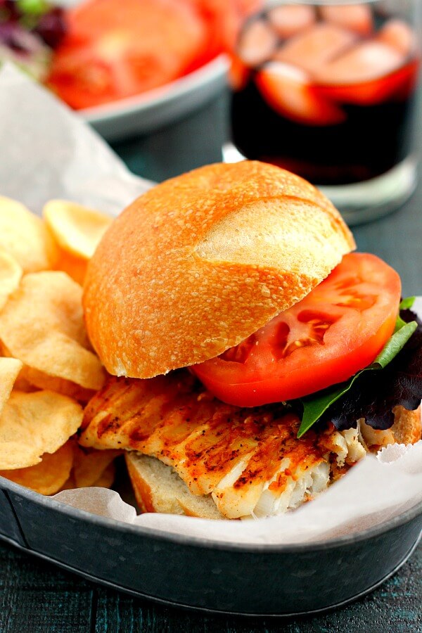 A grilled haddock sandwich on in a sandwich boat with potato chips.