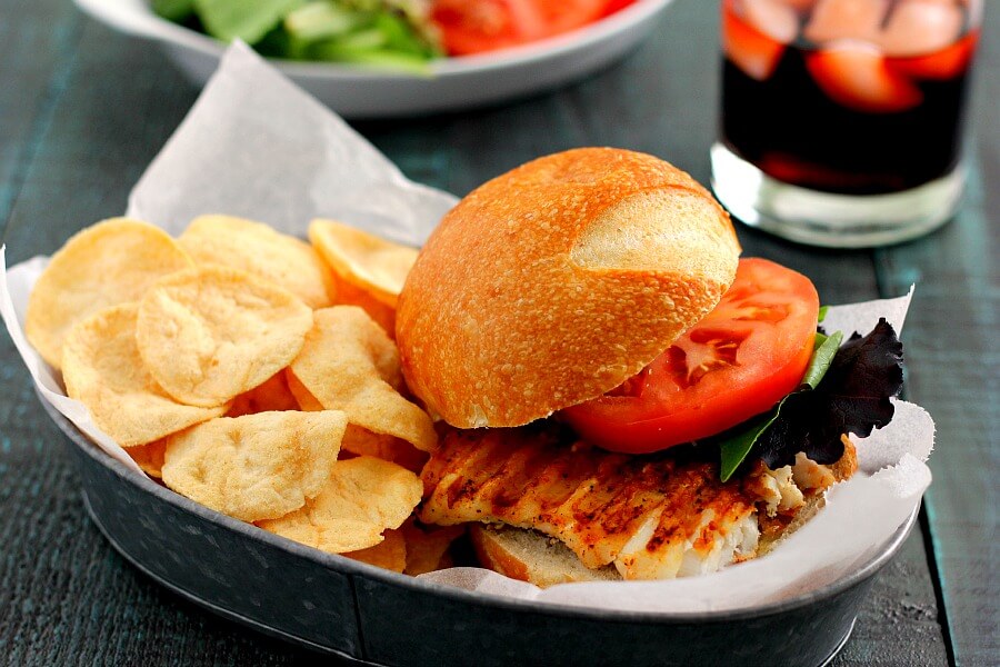 A haddock sandwich on in a sandwich boat with potato chips.