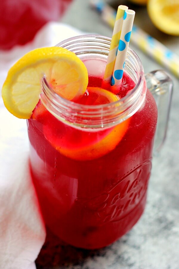 A glass mason jar of homemade blueberry lemonade, garnished with a lemon slice and two paper straws. 