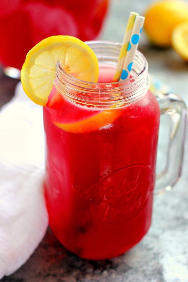 A glass mason jar of homemade blueberry lemonade, garnished with a lemon slice and two paper straws. 