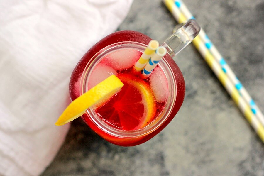 A glass mason jar of homemade blueberry lemonade, garnished with a lemon slice and two paper straws. 