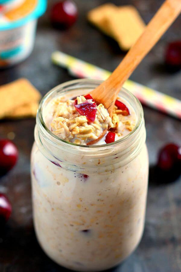 A mason jar filled with cherry overnight oats, with a wooden spoon sticking out. 