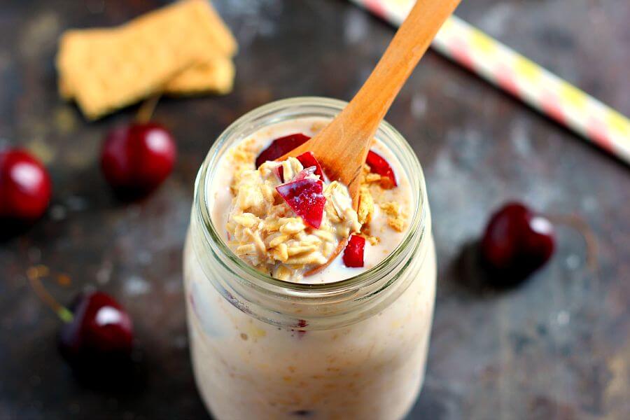 A mason jar filled with cherry overnight oats, with a wooden spoon sticking out. 