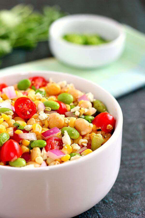 Jam-packed with corn, edamame, chickpeas, and tomatoes, this Corn, Edamame, and Chickpea Salad is full of flavor and makes the perfect light lunch or dinner. By adding a touch of feta cheese, red onion, cilantro, lime juice, and a white balsamic dressing, the ingredients blend together to make a zesty dish!