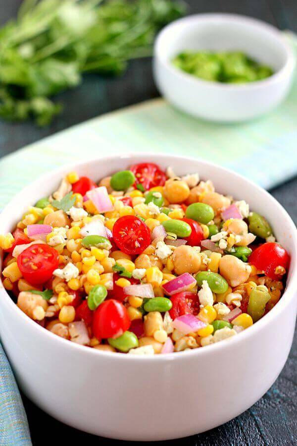 Jam-packed with corn, edamame, chickpeas, and tomatoes, this Corn, Edamame and Chickpea Salad is full of flavor and makes the perfect light lunch or dinner! #salad #saladrecipe #corn #cornsalad #edamame #chickpeas #chickpeasalad #tomatoes #tomatosalad #easysalad #healthysalad #summersalad