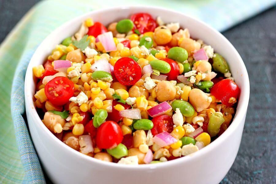 Jam-packed with corn, edamame, chickpeas, and tomatoes, this Corn, Edamame, and Chickpea Salad is full of flavor and makes the perfect light lunch or dinner. By adding a touch of feta cheese, red onion, cilantro, lime juice, and a white balsamic dressing, the ingredients blend together to make a zesty dish!