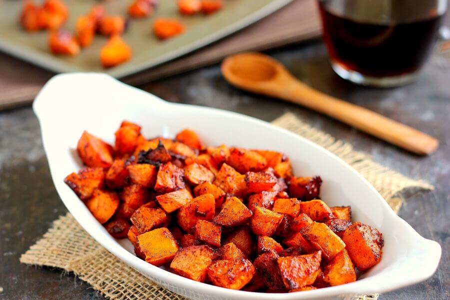 cinnamon sweet potatoes in a white serving dish. A wooden spoon rests in the background. 