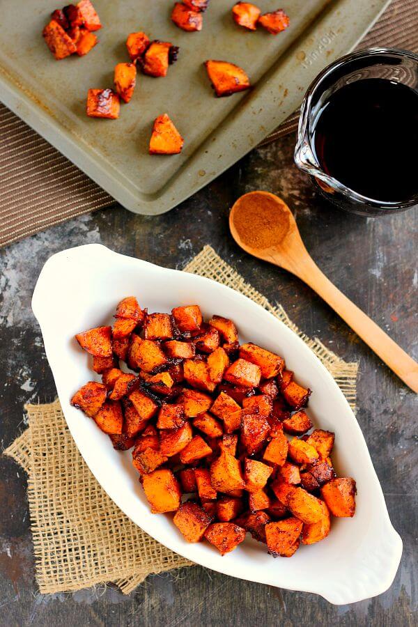 overhead view of sweet potatoes with maple syrup and cinnamon in a white dish. A wooden spoon rests nearby. 