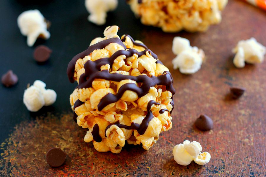 a caramel popcorn ball on a countertop surrounded by popped popcorn 