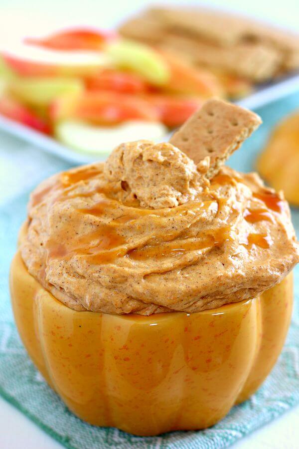 pumpkin cheesecake dip in a pumpkin-shaped serving bowl. a graham cracker sticks out of the top. 