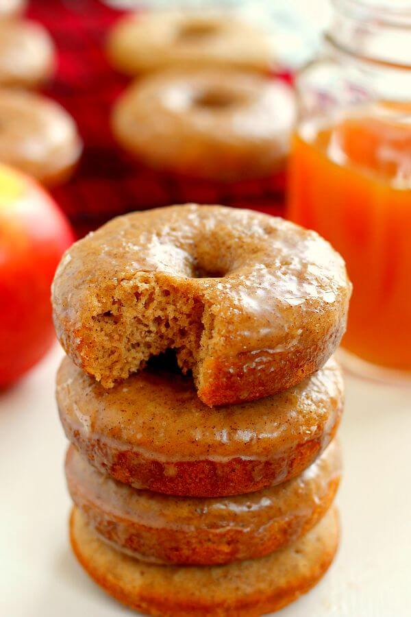 A stack of baked apple cider cake donuts. The top donut has a bite missing. 