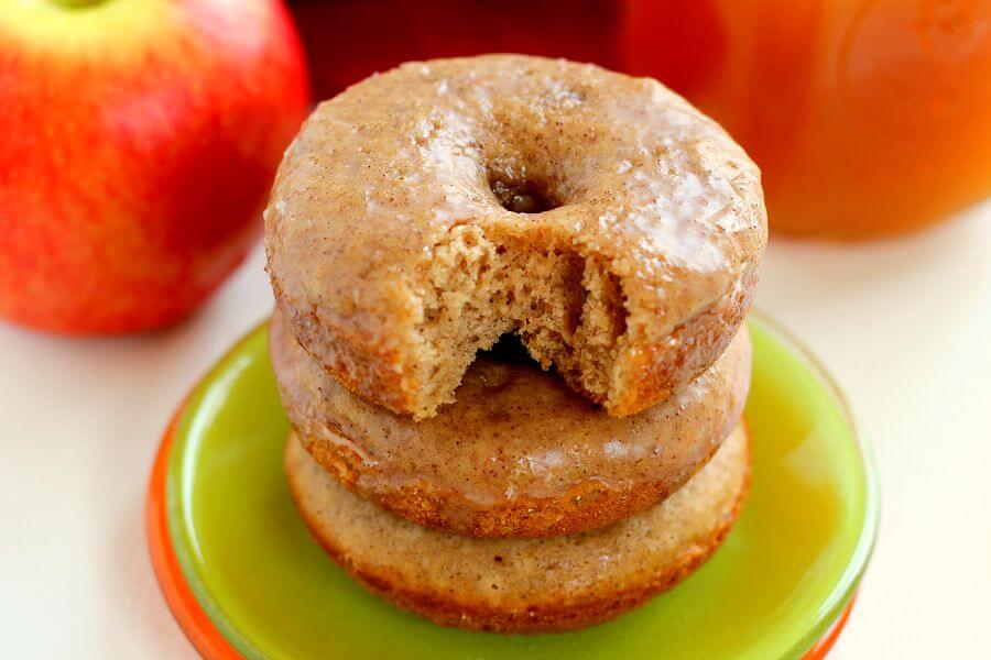 A stack of three baked apple cider donuts with the top donut missing a bite. 
