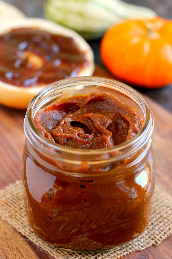 glass jar of pumpkin butter. a bagel slice is in the background 