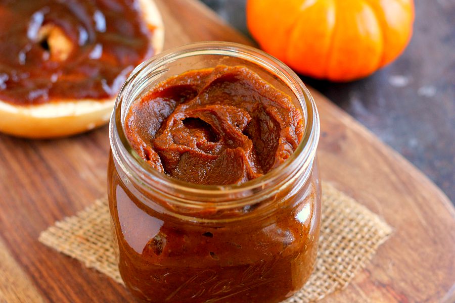 glass jar full of pumpkin butter sitting on wood serving board