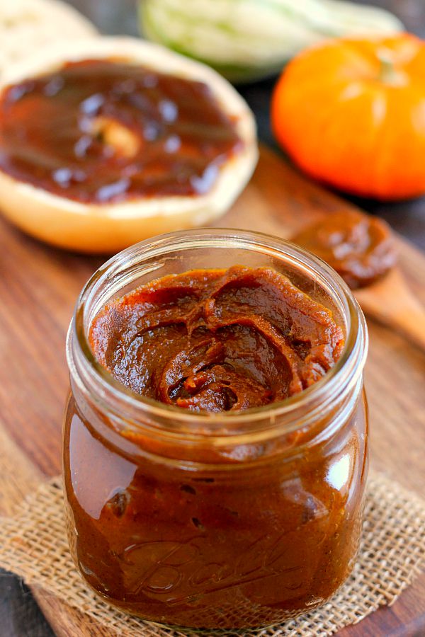 close up of jar of pumpkin butter with spoon and bagel slice in the background