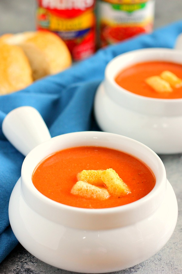 Two ramekins filled with creamy tomato basil soup, garnished with croutons. 