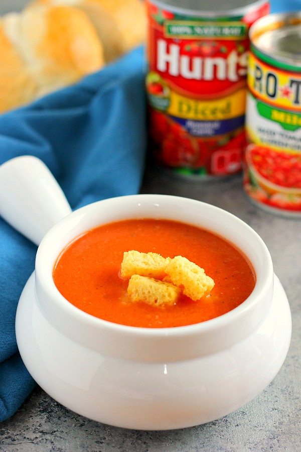 Tomato soup in a white bowl, with canned tomatoes in the background. 