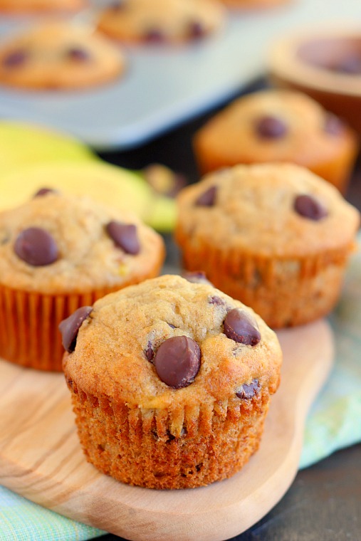Three banana chocolate chip muffins on a wood serving platter. 