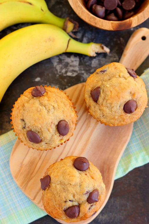 Overhead view of three banana and chocolate chip muffins on a wood serving platter. 