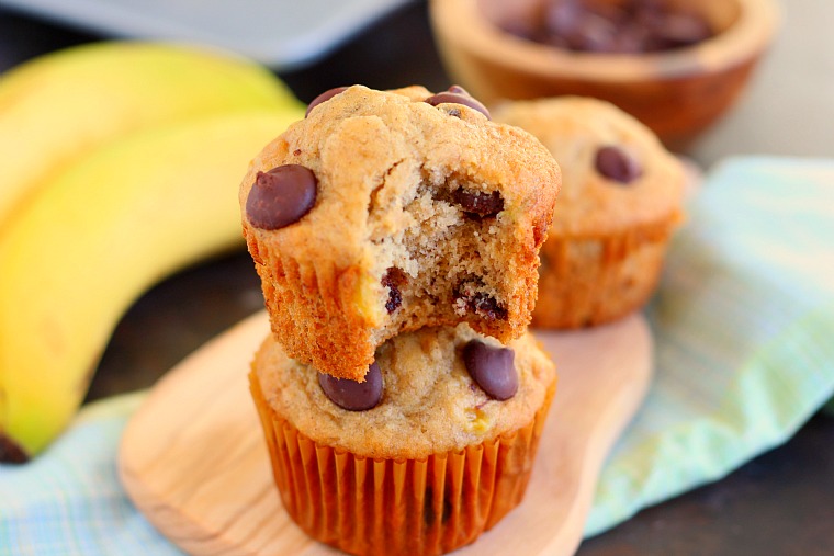 Two banana and chocolate chip muffins stacked on each other. The top muffin has a bite missing. 