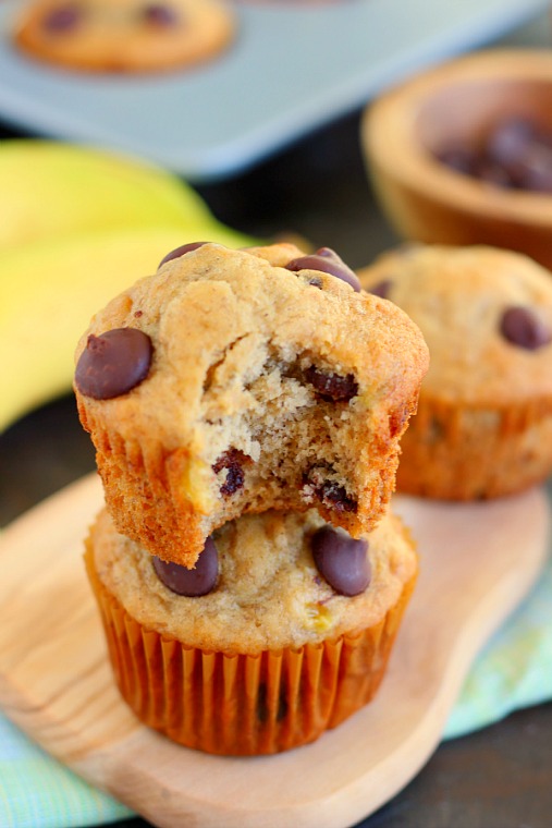 Two banana and chocolate chip muffins stacked on each other. The top muffin has a bite missing. 