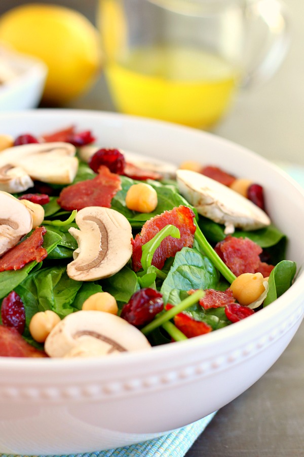 This Cranberry Mushroom Spinach Salad with Lemon Basil Vinaigrette combines baby spinach leaves, dried cranberries, fresh mushrooms, chickpeas, and crumbled bacon, all tossed with a lemon basil dressing. This dish is easy to throw together and serves as the perfect lunch or dinner! #spinachsalad #cranberries #mushroom #mushroomsalad #cranberrysalad #saladrecipes #healthysalad #thanksgiving #lunch 