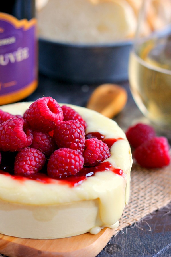 easy baked brie topped with jam and berries on a wood board 