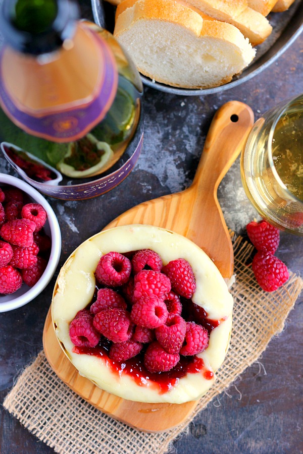 overhead view of baked brie with raspberry jam and fresh berries and a bottle of wine 