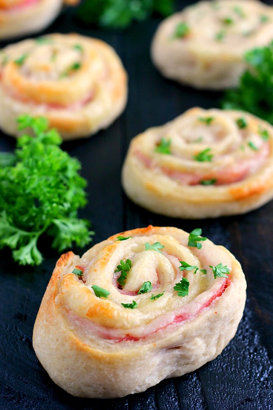Ham and cheese roll ups on a gray surface, with fresh parsley. 