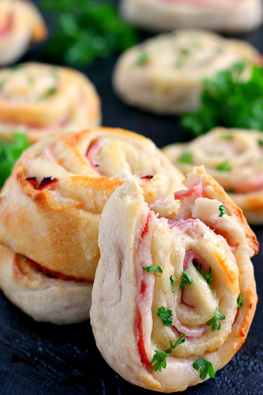 A stack of baked ham and cheese roll ups, with one roll ups leaning against it. 