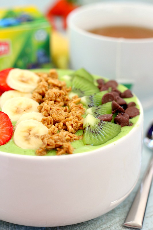 a tropical green smoothie bowl with various toppings. a mug of Lipton tea rests in the background. 