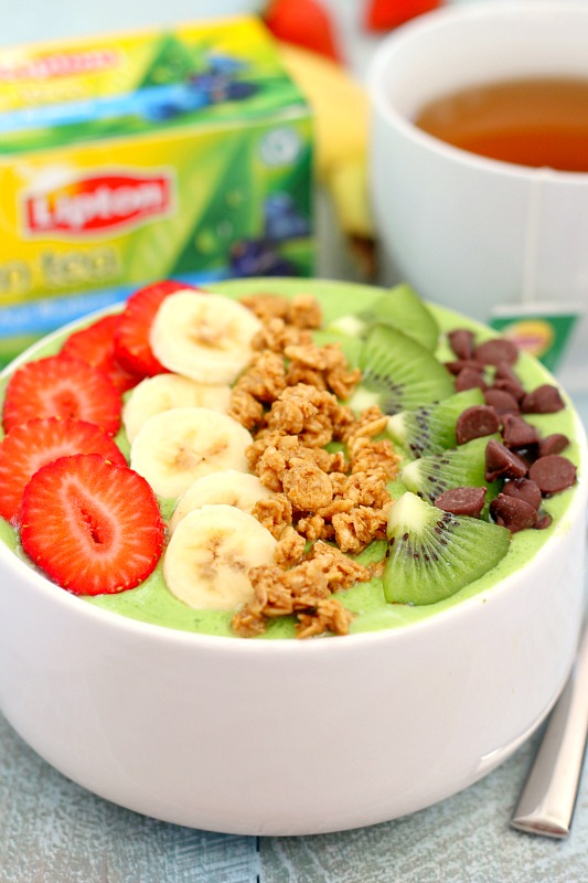 a tropical green smoothie bowl with various toppings. a mug of Lipton tea rests in the background. 