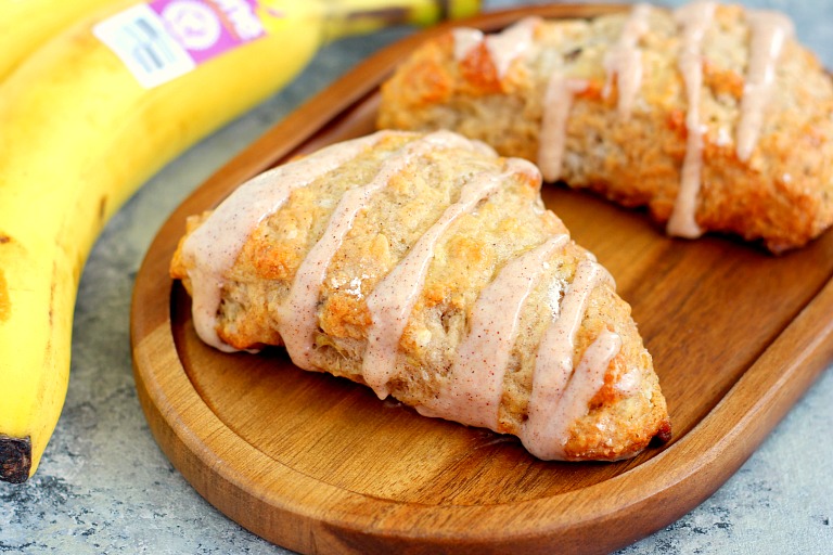 two glazed banana bread scones on a wood board next to a banana 