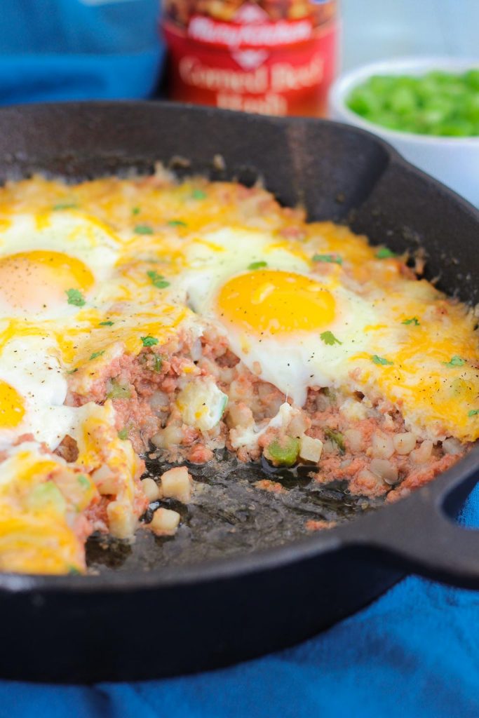 canned corned beef hash and eggs in a cast iron skillet. A portion has been scooped out. 