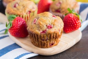 a strawberry banana muffin on a cutting board surrounded by strawberries