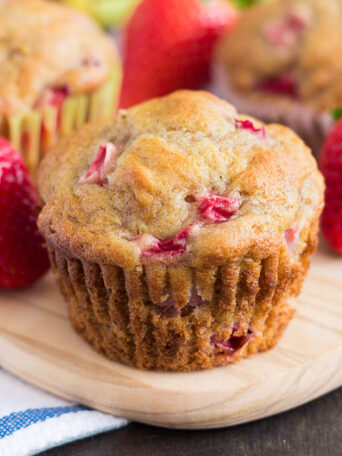 a strawberry banana muffin on a cutting board surrounded by strawberries