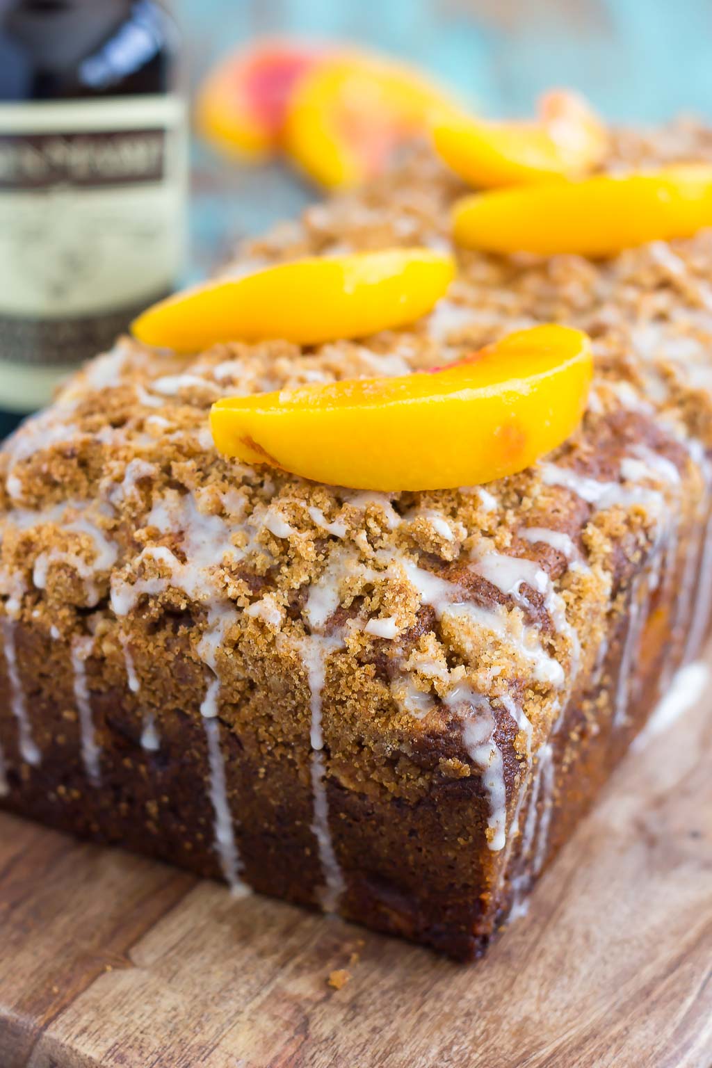 A loaf of glazed peach streusel bread on a wooden cutting board.