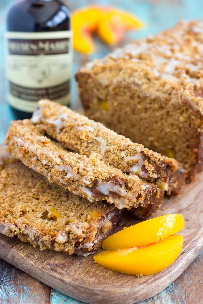 A sliced loaf of peach bread on a wood cutting board. A bottle of vanilla bean paste rests in the background. 