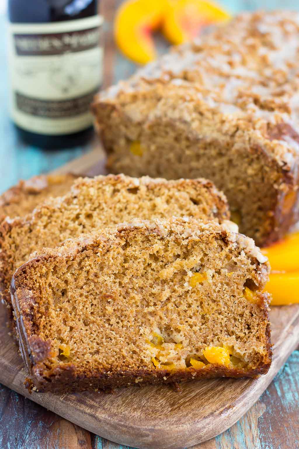 A sliced loaf of peach bread on a wood cutting board. A bottle of vanilla bean paste rests in the background.