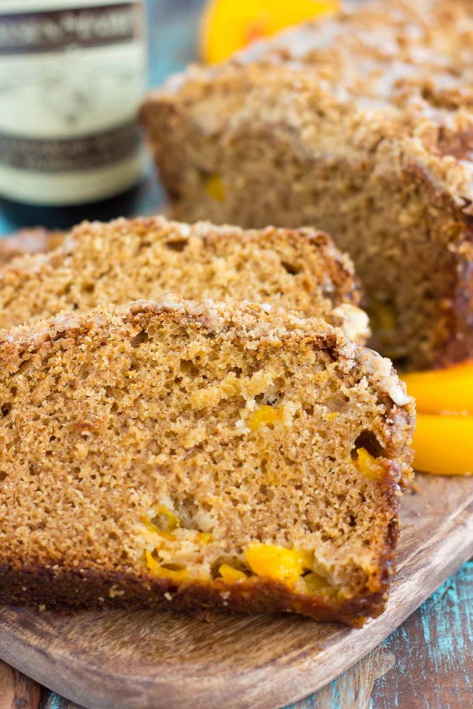 A sliced loaf of peach bread on a wood cutting board. A bottle of vanilla bean paste rests in the background. 