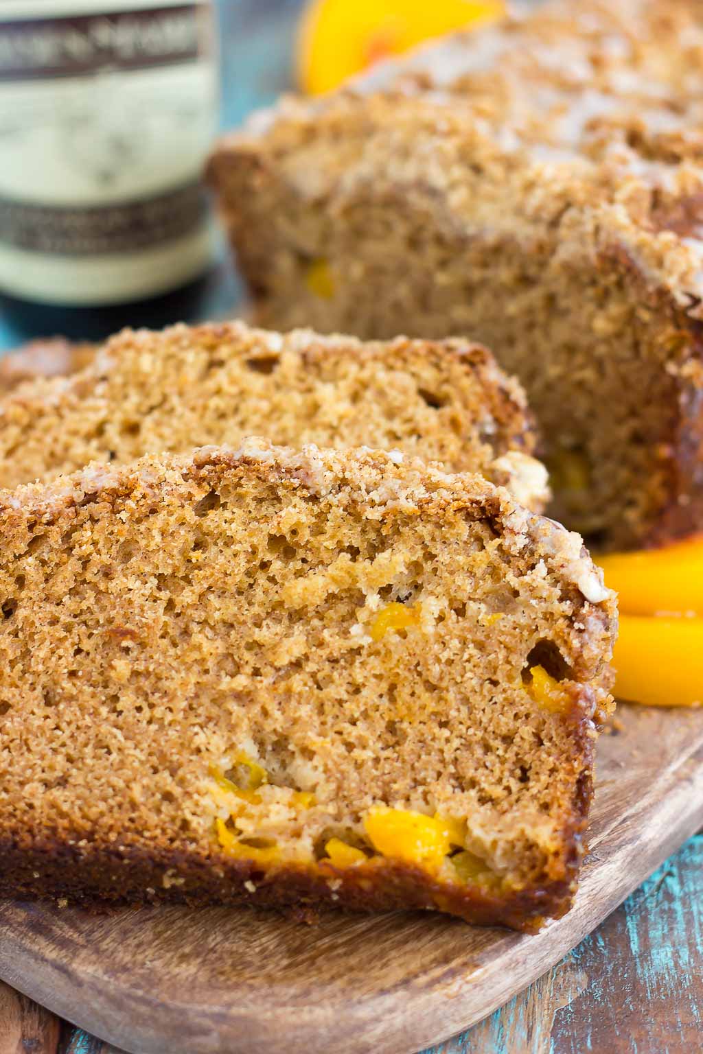 A sliced loaf of peach bread on a wood cutting board. A bottle of vanilla bean paste rests in the background.
