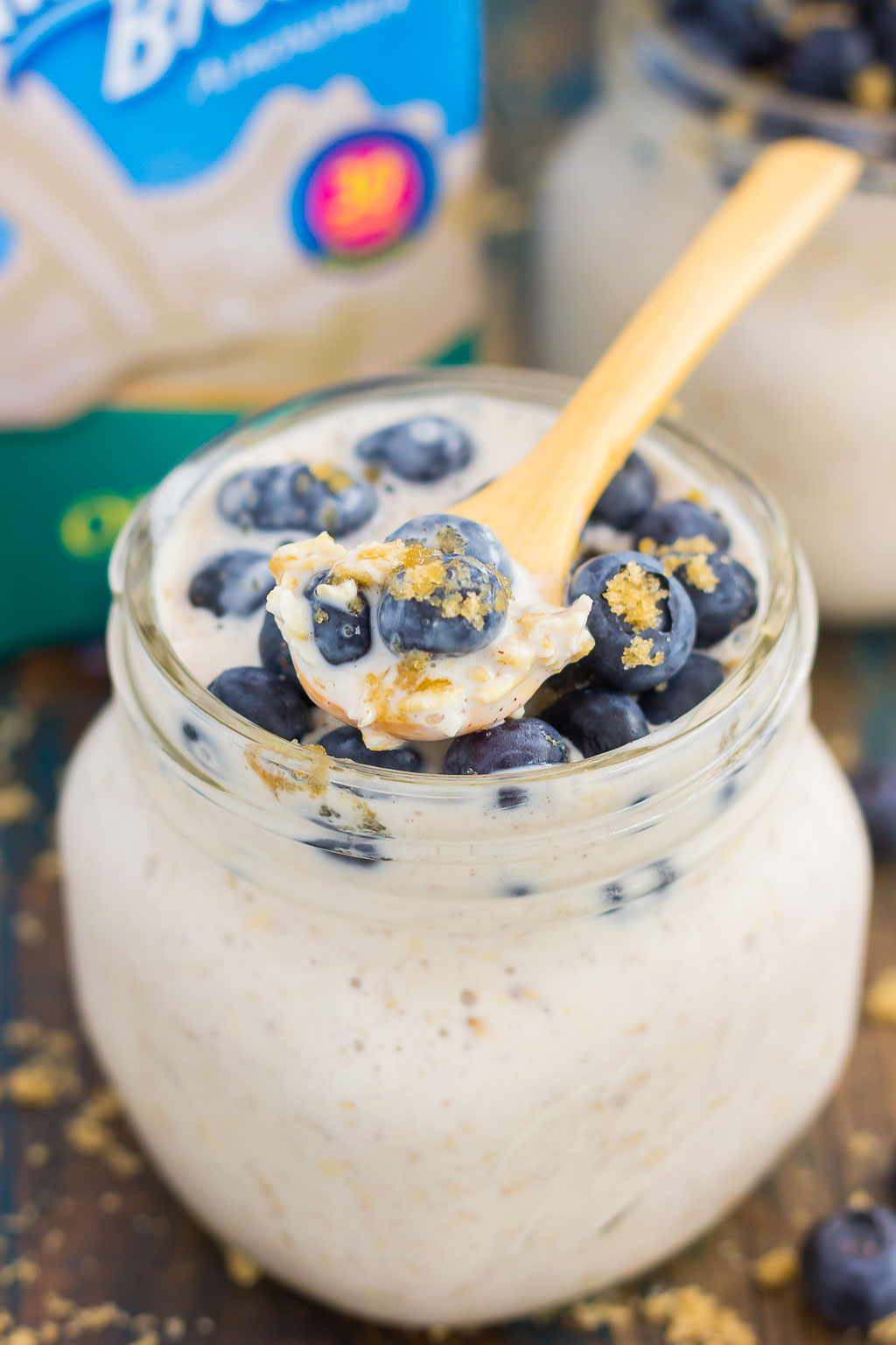 A jar of blueberry overnight oats. A small wooden spoon rests on top of the jar.