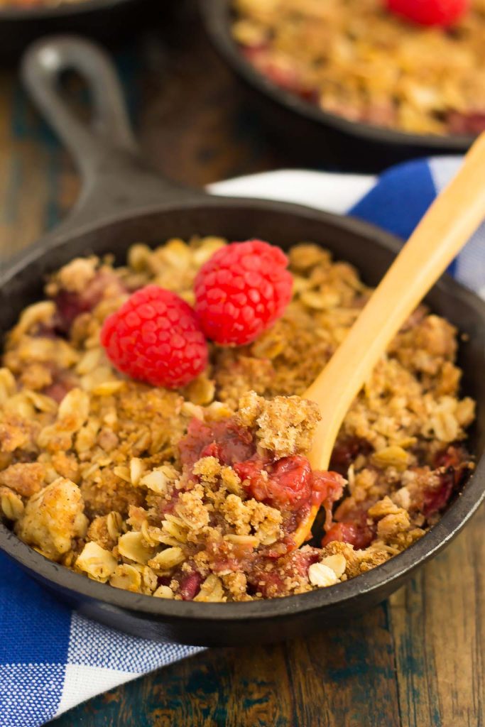 A mini skillet of rhubarb raspberry crisp, with a wooden spoon. 