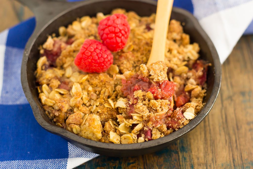 A mini skillet of rhubarb raspberry crisp, with a wooden spoon. 